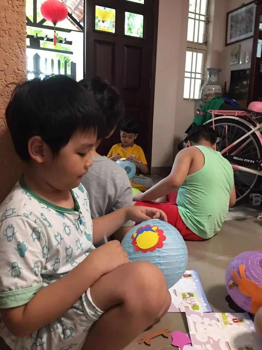 Đèn lồng Trung Thu — Bé tỉ mẩn dán hình lên chiếc đèn lồng giấy của mình ngay tại phòng khách.